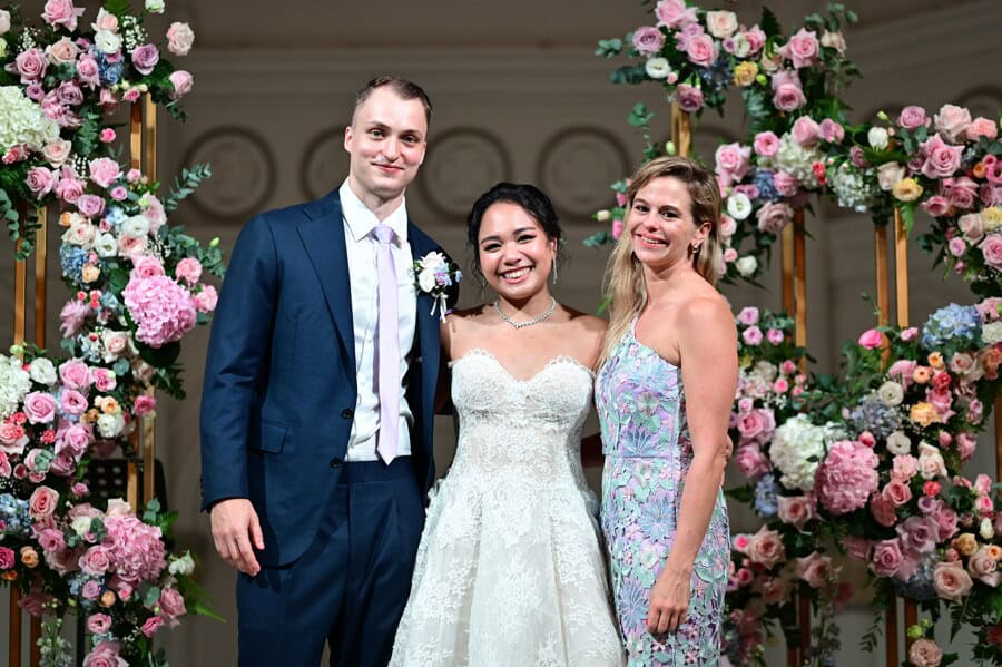 Daniela Erni of Create Your Story with couple Abelle and Florian after their Bridgerton-inspired wedding ceremony at CHIJMES Singapore, surrounded by lush multi-colour floral pillar installations in pink roses, blue hydrangea and white blooms
