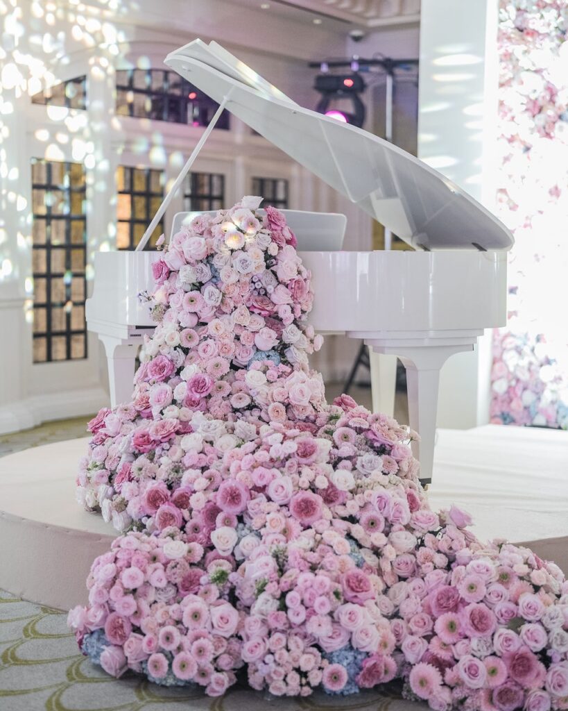 White grand piano submerged in thousands of blush and pink roses and ranunculus ~ luxury wedding floral installation at Raffles Hotel Singapore ~ design by Tomas De Bruyne and Create Your Story