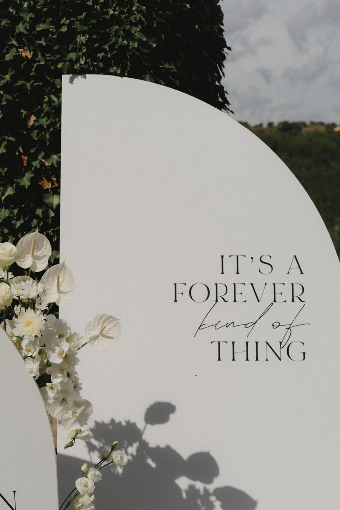 espoke circular wedding welcome sign with white anthurium and orchid floral arrangement and handwritten typography — Valérie & Björn destination wedding, custom stationery and floral design by Create Your Story, Umbria Italy 2024